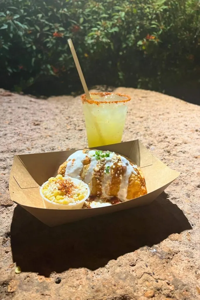 Photo of a basket with empanada de barbacoa and a cup of corn esquites with a margarita in the background.