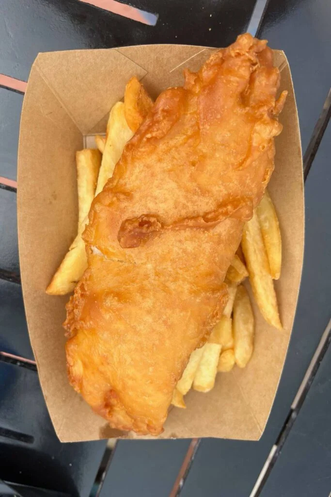 Photo of a basket of a hunk of fried fish on top of french fries.