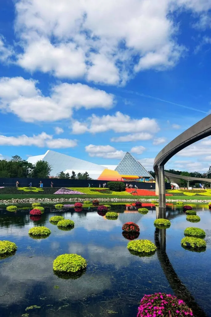 Photo of the pyramid that houses Journey into Imagination with Figment ride from across a lake, with clouds reflecting in the water.