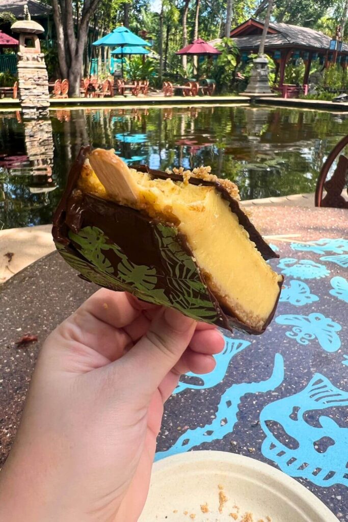 Photo of the key lime pie pop from Flame Tree Barbecue, with a few bites taken out of it, with a beautiful garden, statues, and a pool in the background.