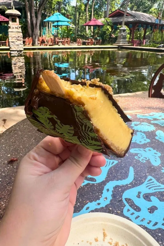 Photo of the key lime pie pop from Flame Tree Barbecue, with a few bites taken out of it, with a beautiful garden, statues, and a pool in the background.