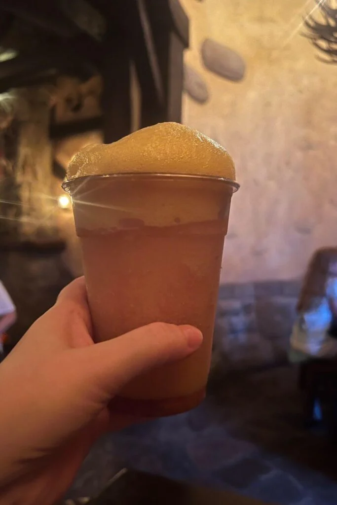 Photo of the frozen Lefou's Brew, a frozen apple drink with a passionfruit foam topping inside Gaston's Tavern at Magic Kingdom.