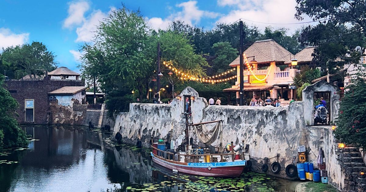 Photo of Discovery River nearby the Africa section of Disney's Animal Kingdom, with a boat in the water and string lights glowing in the background.