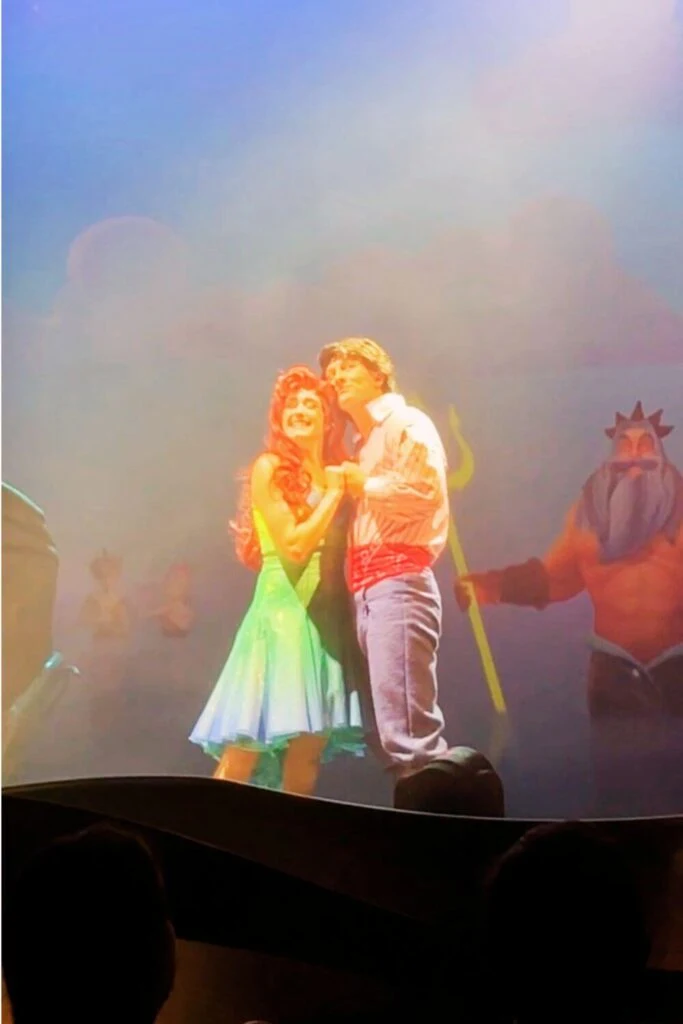 Photo of Ariel and Eric from The Little Mermaid: A Musical Adventure dancing, while Triton watches in the background.