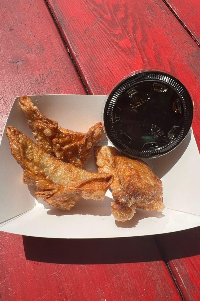 Photo of 3 crispy fried chicken potstickers in a basket with a cup of ponzu dipping sauce.