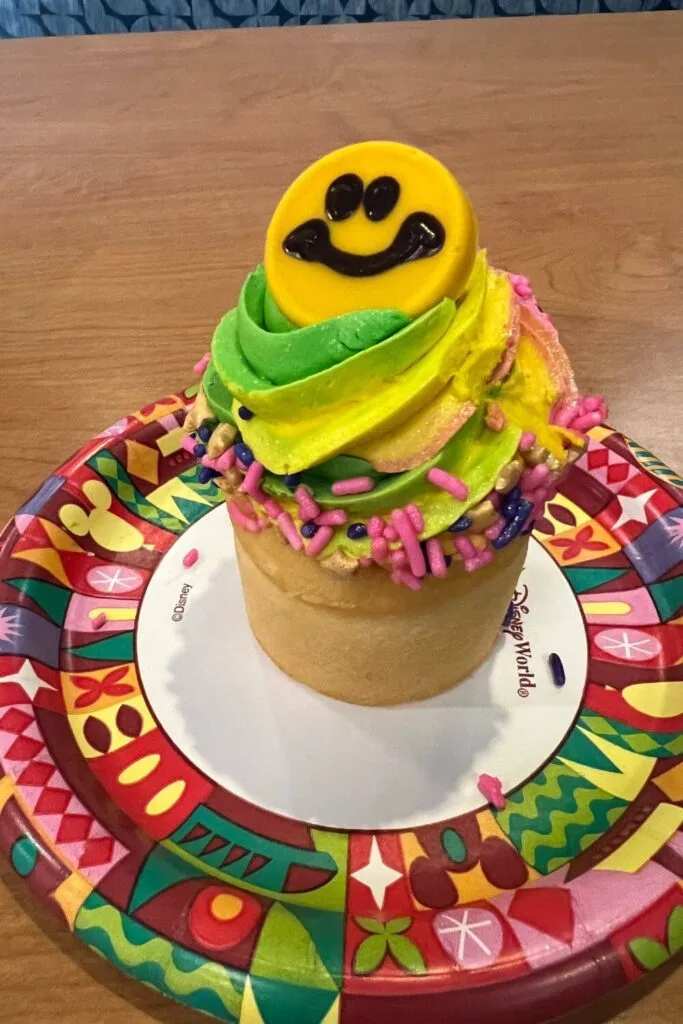 Photo of the Pop Goes Bananas cupcake with tie-dye frosting and a smiley face chocolate coin from Pop Century Resort at Disney World.