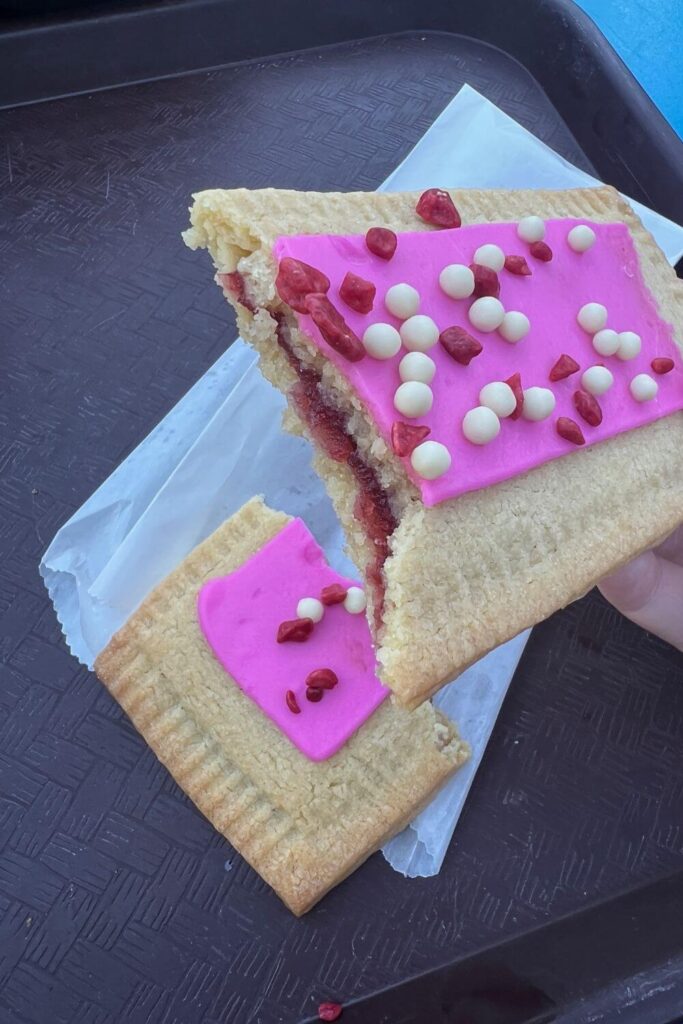 Closeup of a raspberry lunchbox tart with pink frosting broken in half to show the jam filling.