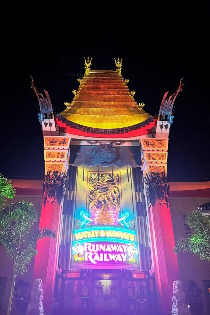 Photo of the exterior of Mickey & Minnie's Runaway Railway ride at Hollywood Studios, lit up in neon lights at night.