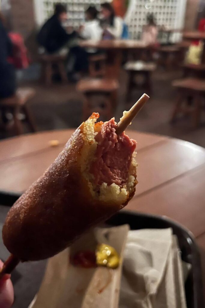 Closeup of a hand dipped corn dog on a stick from Sleepy Hollow, half eaten.