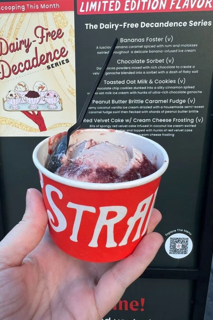 Photo of a cup of strawberry honey balsamic with black pepper ice cream from Salt & Straw in Disney Springs. A sign with a menu of dairy-free options is in the background.