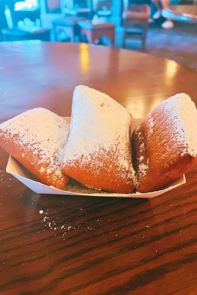 Photo of 3 rectangular beignets covered in powdered sugar, nestled in a basket.