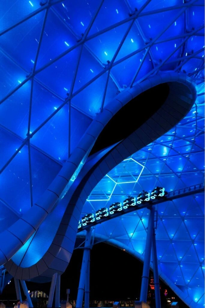 Photo of TRON Lightcycle / Run roller coaster at Magic Kingdom, lit up in blue at night.
