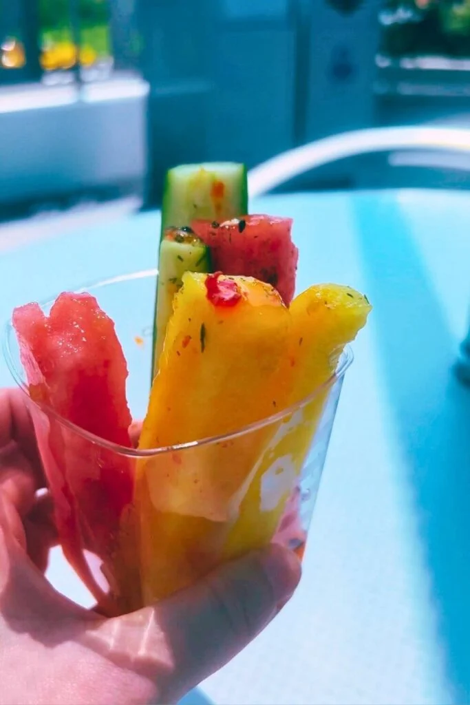 Closeup of a cup of watermelon, pineapple, and cucumber sticks with chili sauce and furikake.